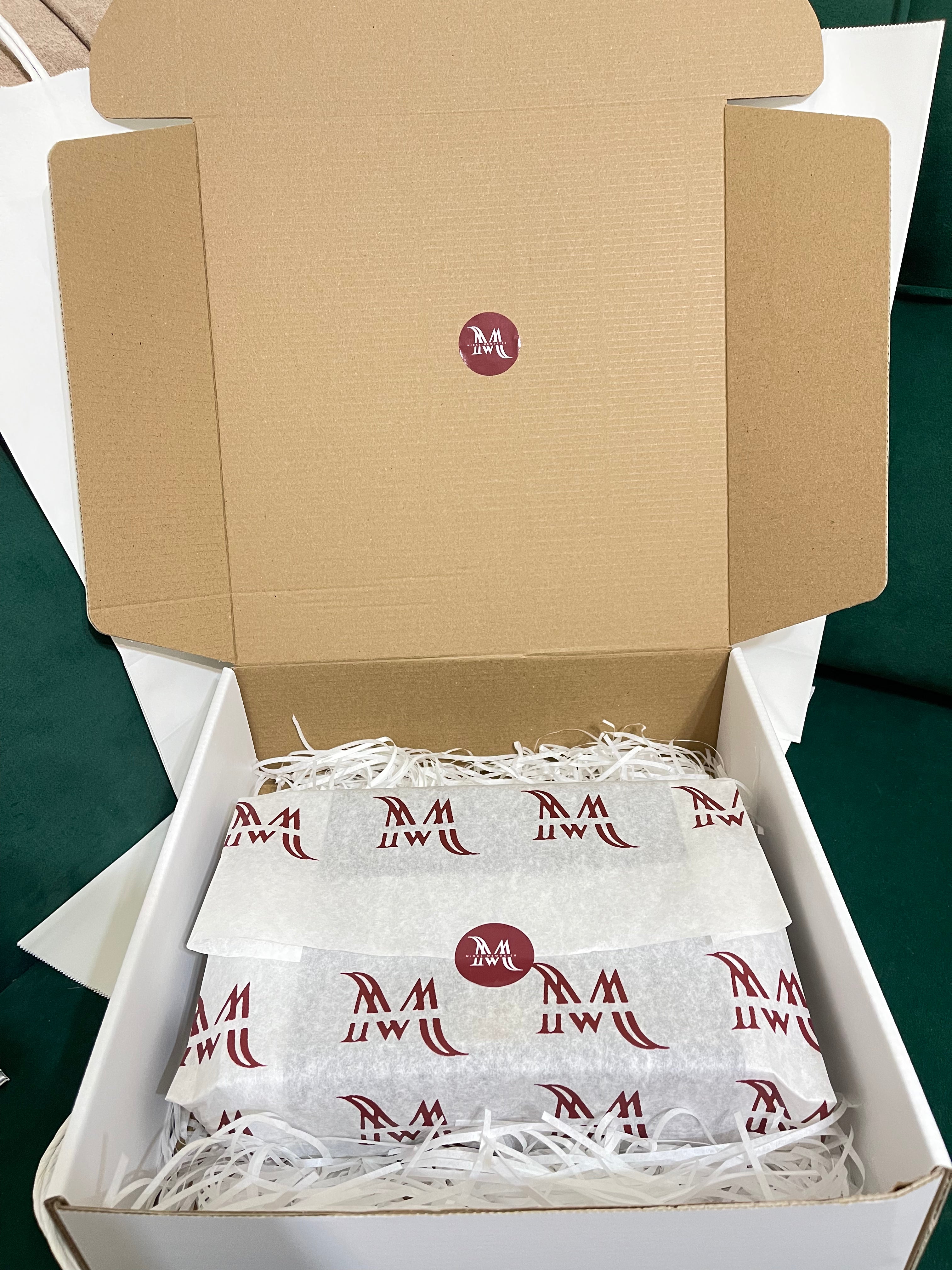 Open box containing white packages with red logo on a green surface