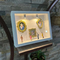 Decorative display case with framed pictures and small figures against a stone wall.