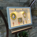 Decorative display case with framed pictures and small figures against a stone wall.