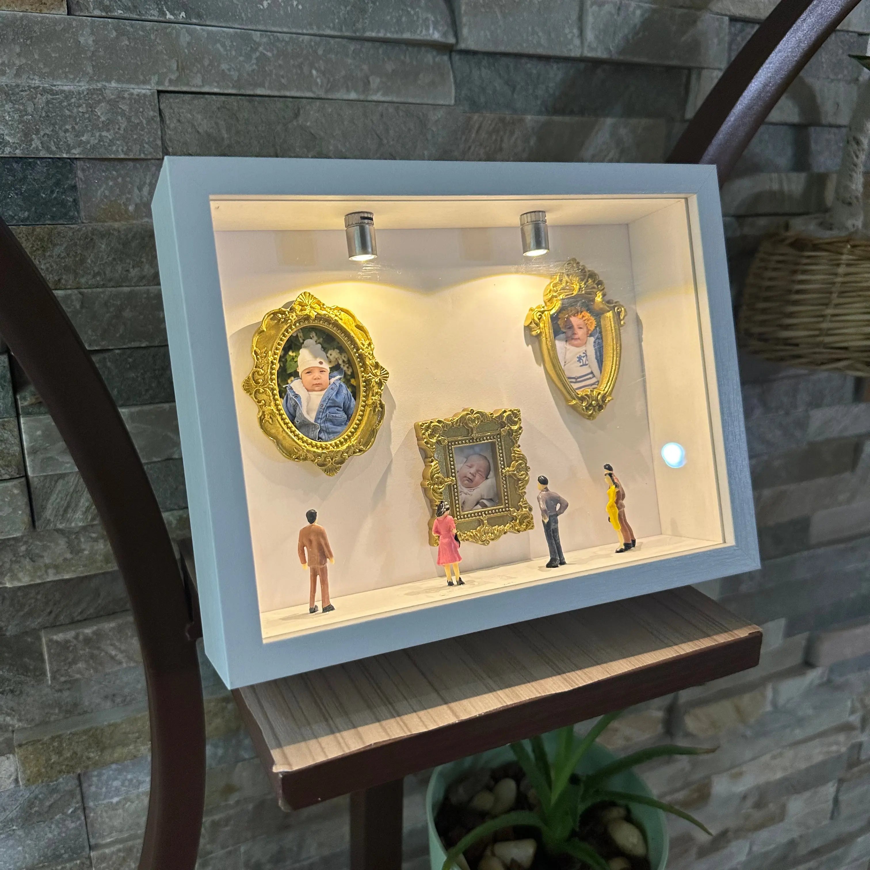 Decorative display case with framed pictures and small figures against a stone wall.