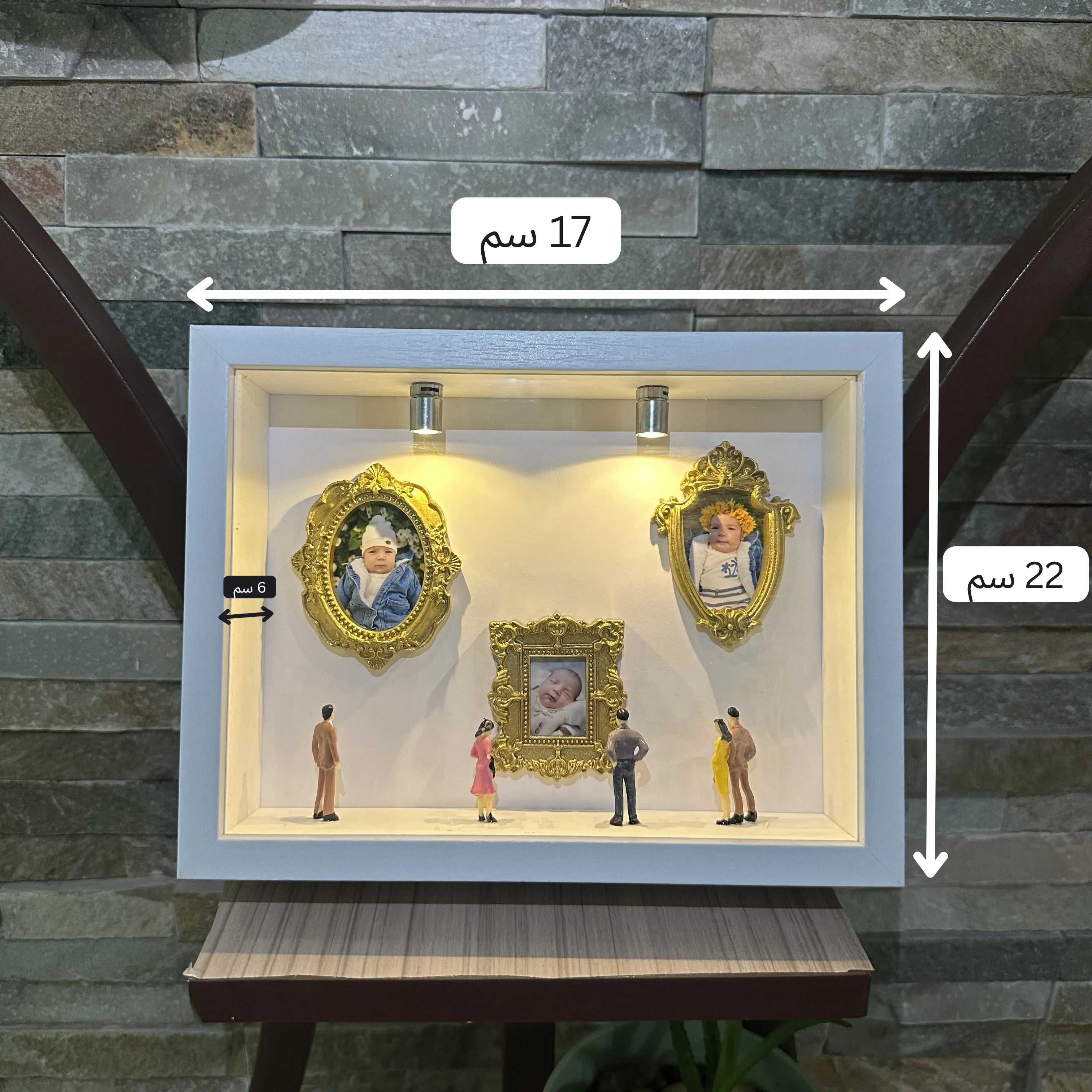 Decorative display case with framed pictures and small figures on a stone wall background